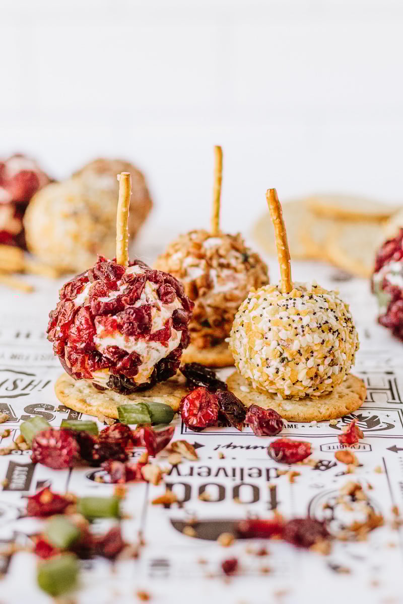 Mini cheeseball appetizers with pretzel sticks on parchment paper.
