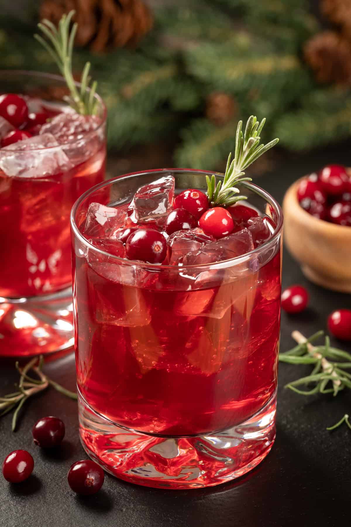 Cranberry spritzer in glass garnished with cranberries and fresh rosemary.