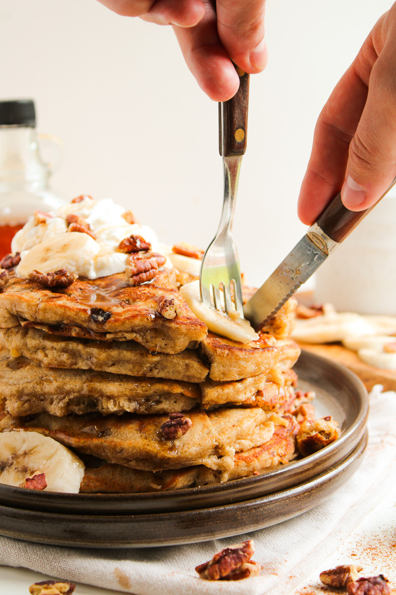 Knife and fork cutting into a stack of banana pancakes.