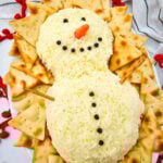 Snowman cheeseball surrounded by crackers on a board.