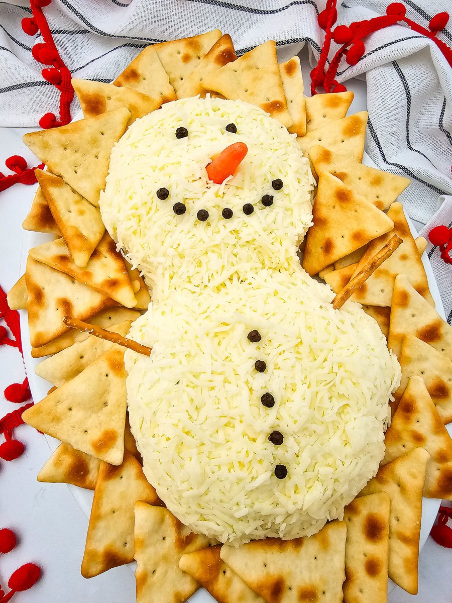 Snowman cheeseball surrounded by crackers on a board.