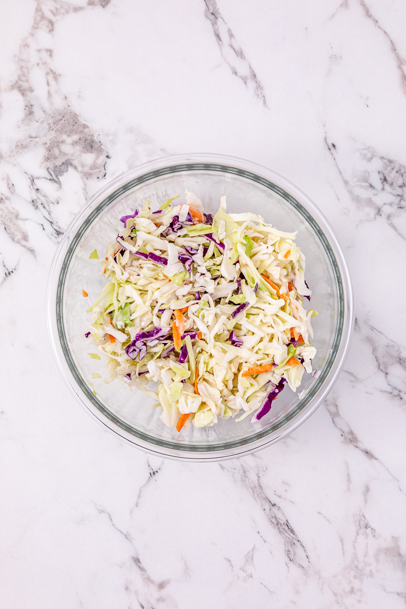 Coleslaw dressing is added to the coleslaw in bowl.