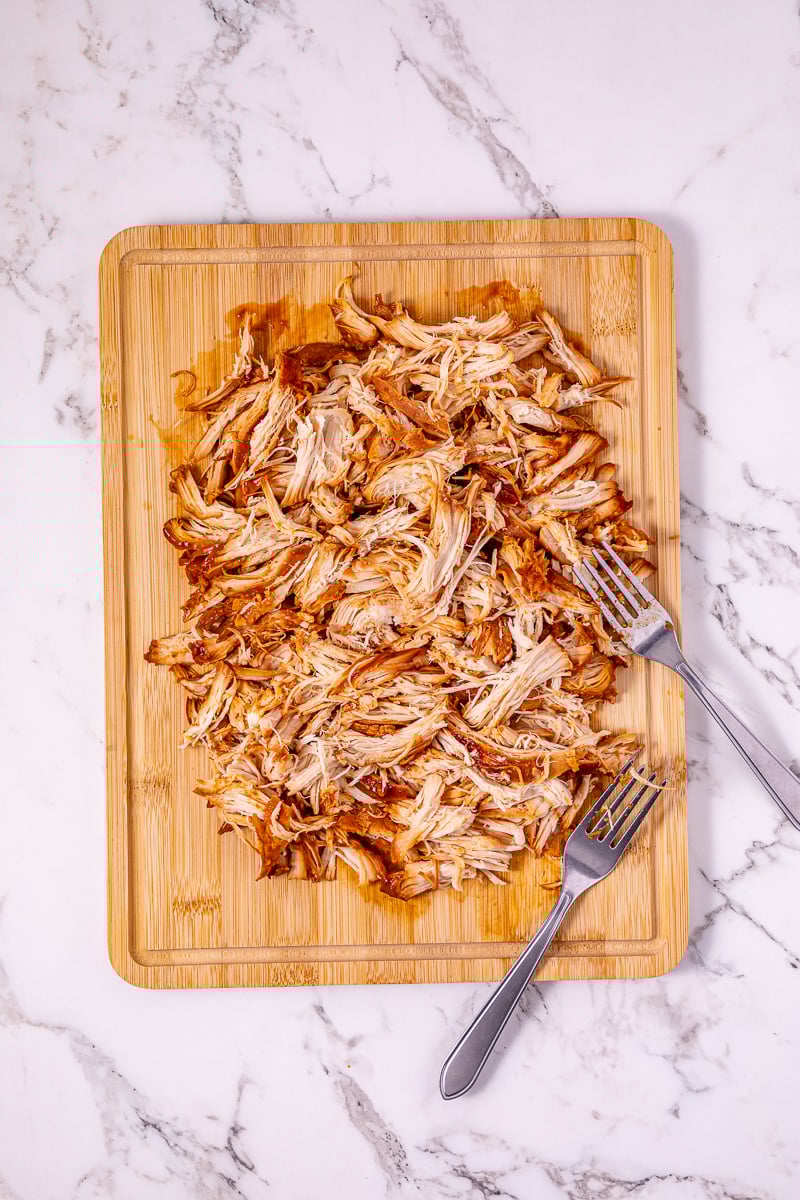 Chicken is placed on cutting board and shredde with two forks.