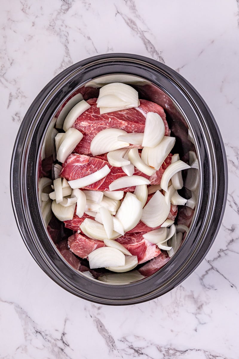 Pork ribs and onions are placed in the crockpot.