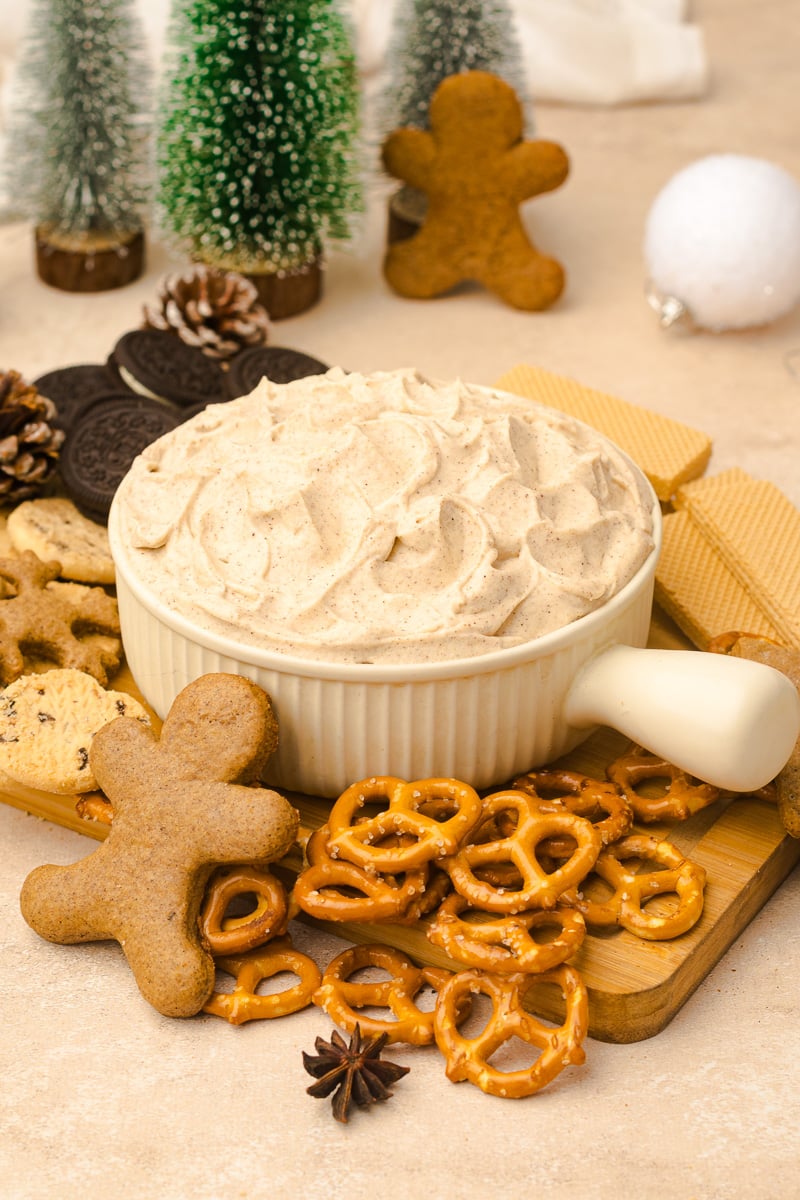 Finished dish of gingerbread cheesecake dip in bowl surrounded by pretzels and gingerbread cookies for dipping.