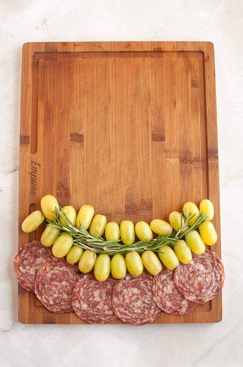 A row of grapes is placed agove the salami.
