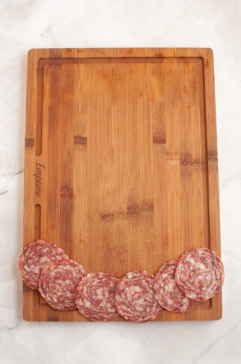 Salami is placed at the bottom of a wooden board.