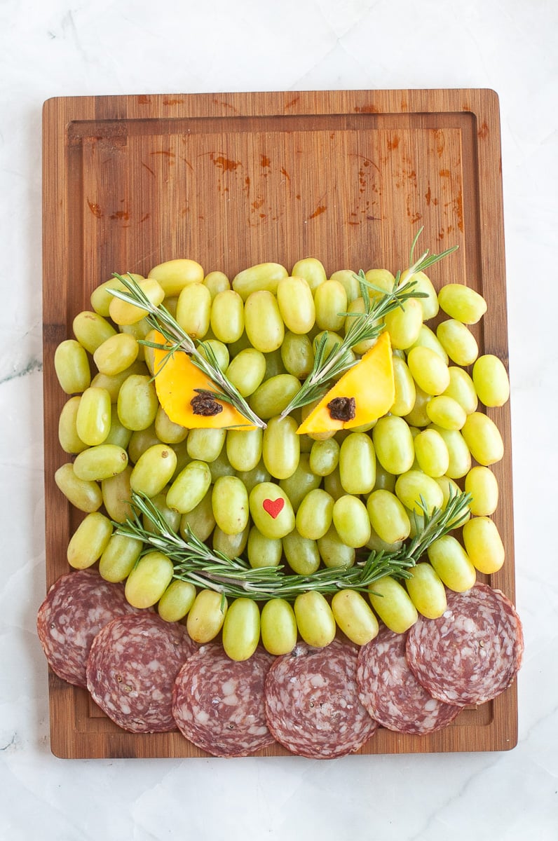 Cheese is placed on the face along with raisins for eyes and heart nose.