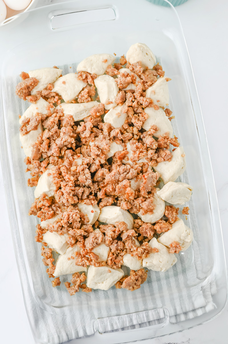 Sausage is sprinkled on top of the biscuits in pan.