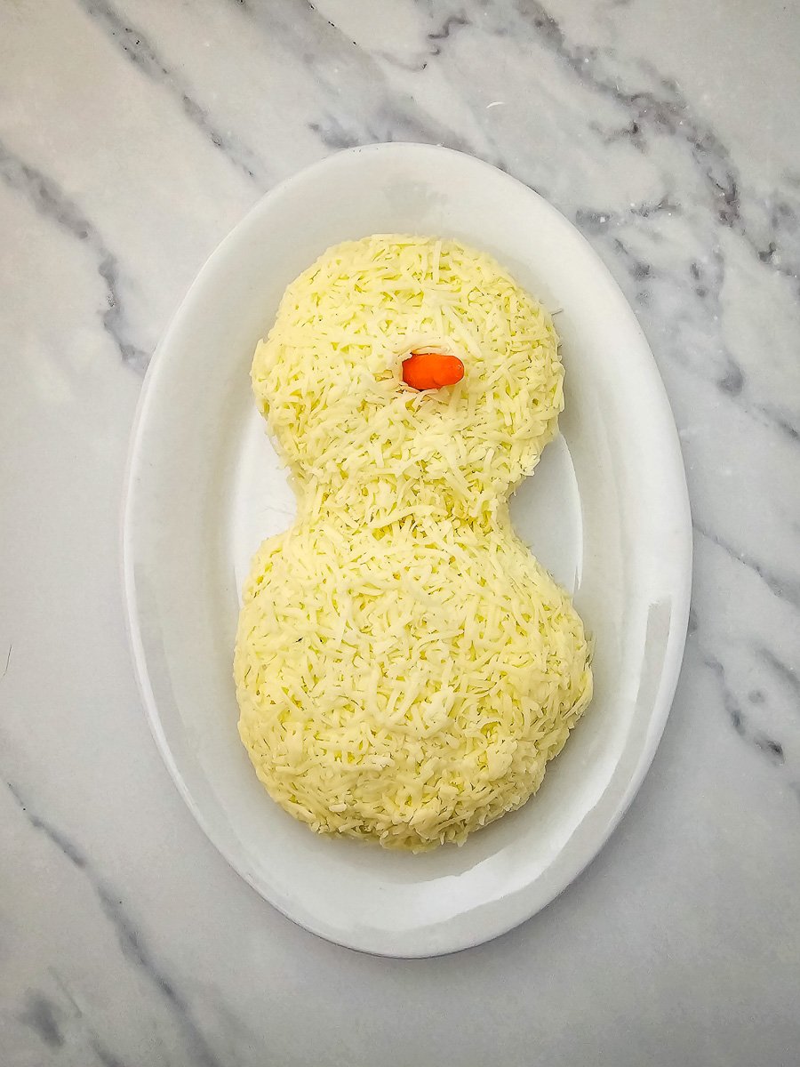 Cheddar cheese is presse dinto the top of the cheeseball and baby carrot nose is added.