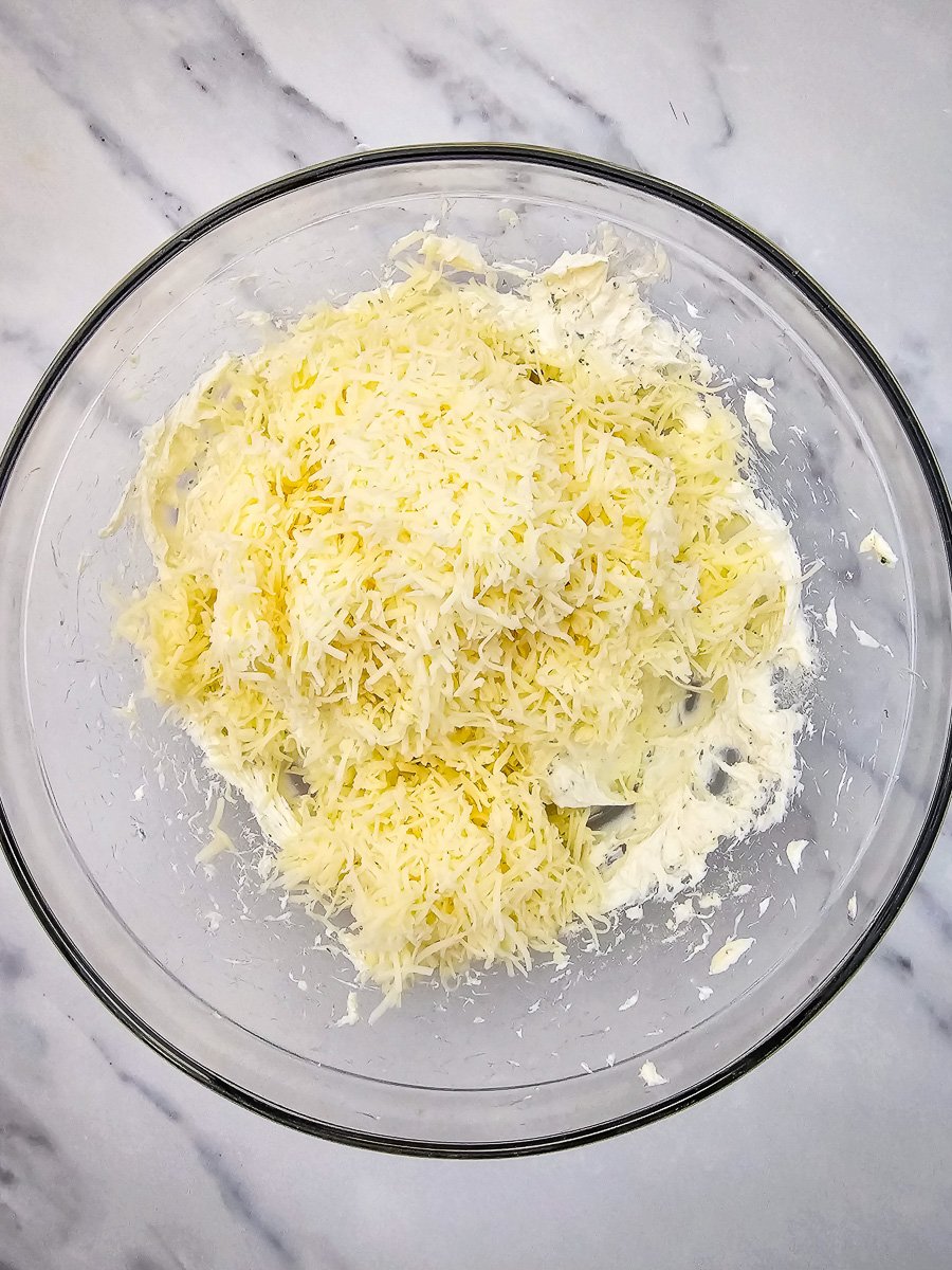 Some of the cheddar is added to cream cheese mixture in mixing bowl.