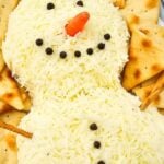 Snowman cheeseball on a serving board surrounded by crackers.