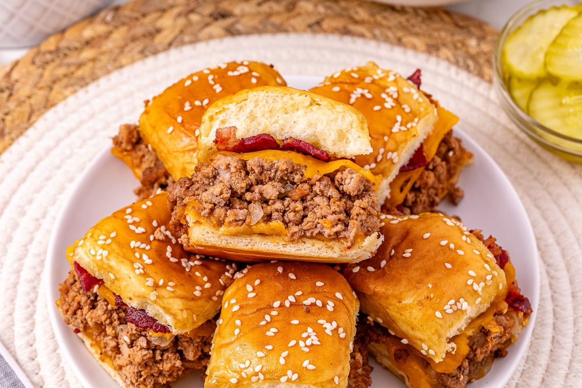 Stack of bacon cheeseburger sliders on plate.