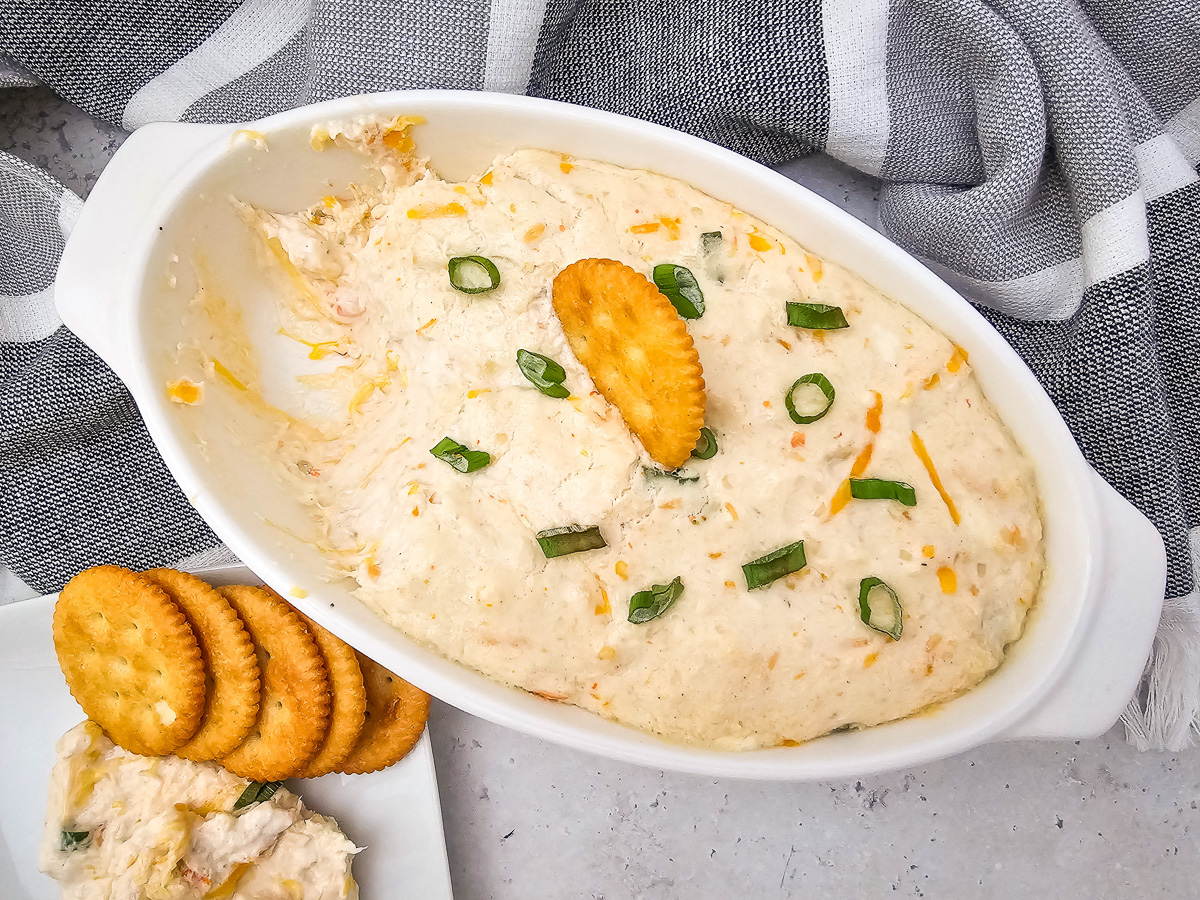 Hot seafood dip in white dish with crackers on the side.