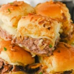 French Dip sliders with Au Jus stacked on a white plate.