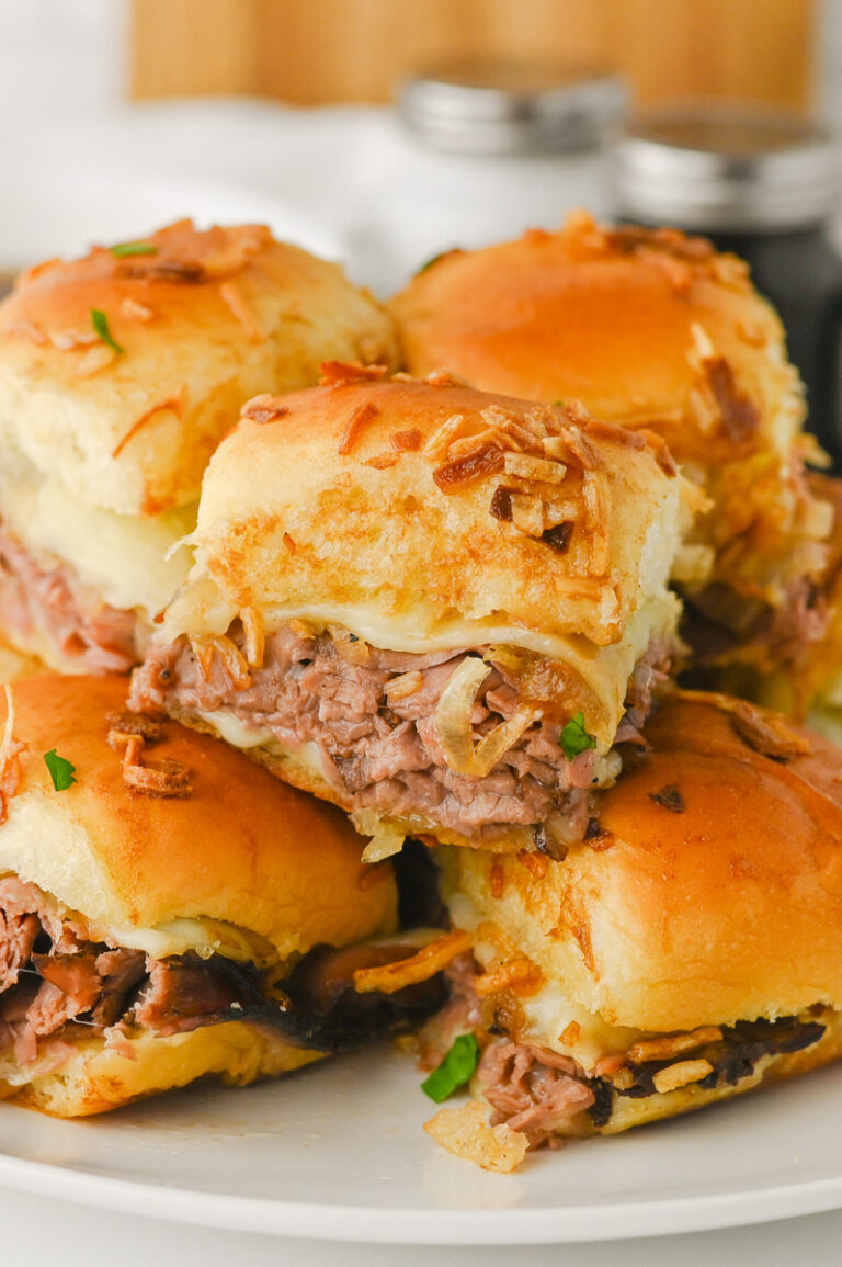 French Dip sliders with Au Jus stacked on a white plate.