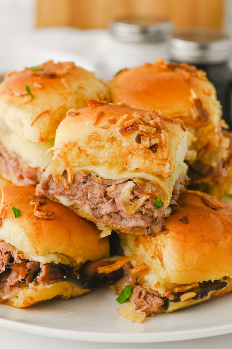 French Dip sliders with Au Jus stacked on a white plate.