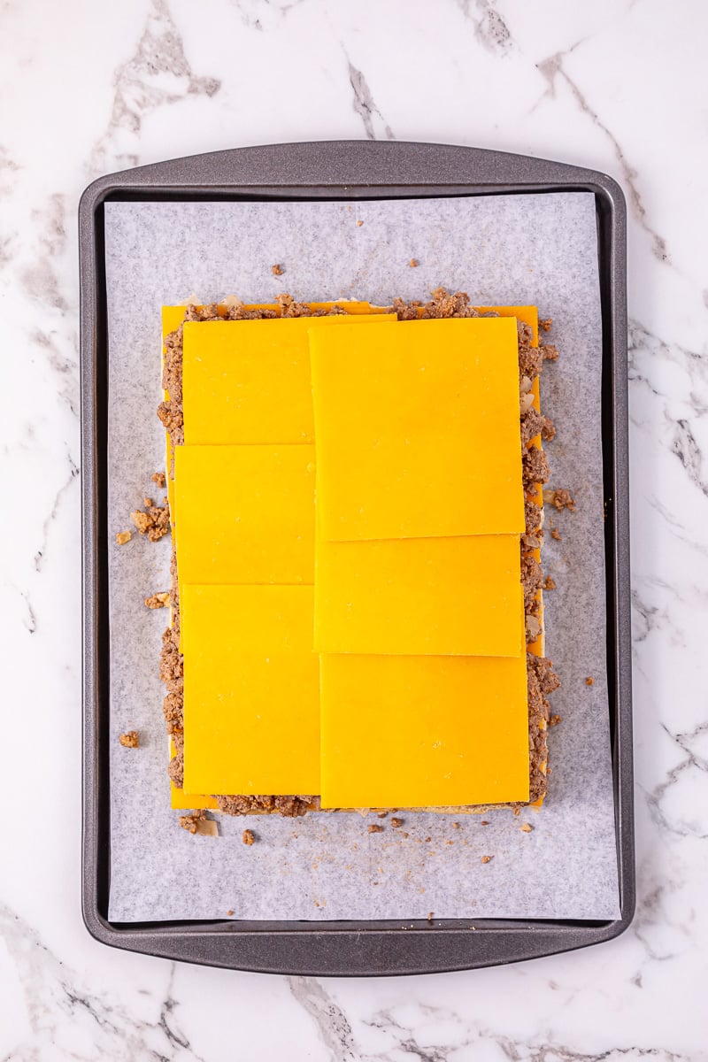 A second cheese layer is placed on top of ground beef.