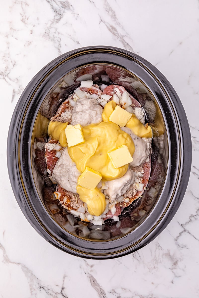 Cream of mushroom soup and cream of chicken soup is added to the top of the pork chop mixture in crockpot.