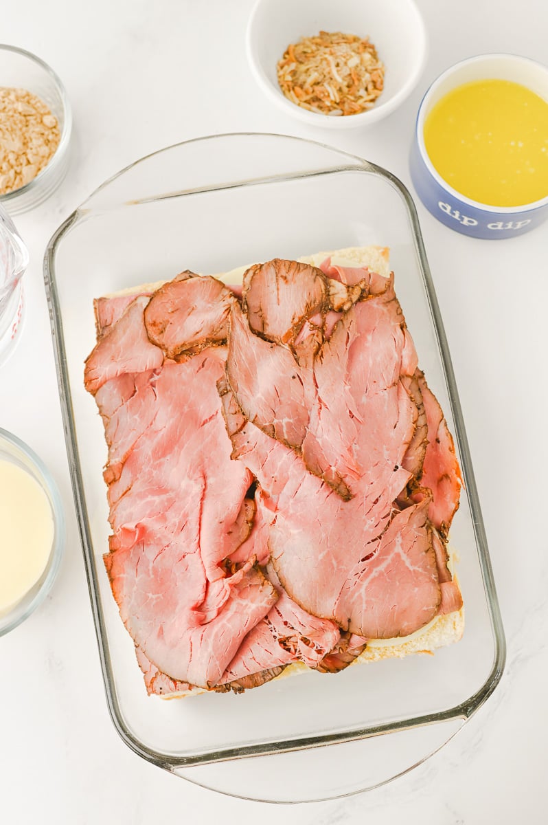 Sliced roast beef is added to the top of provolone cheese on slider buns.