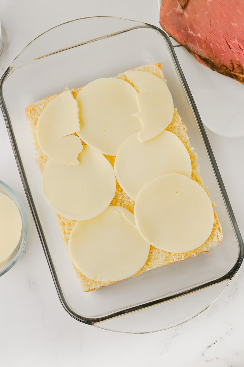 Provolone cheese slices are placed on top of slider buns in baking dish.