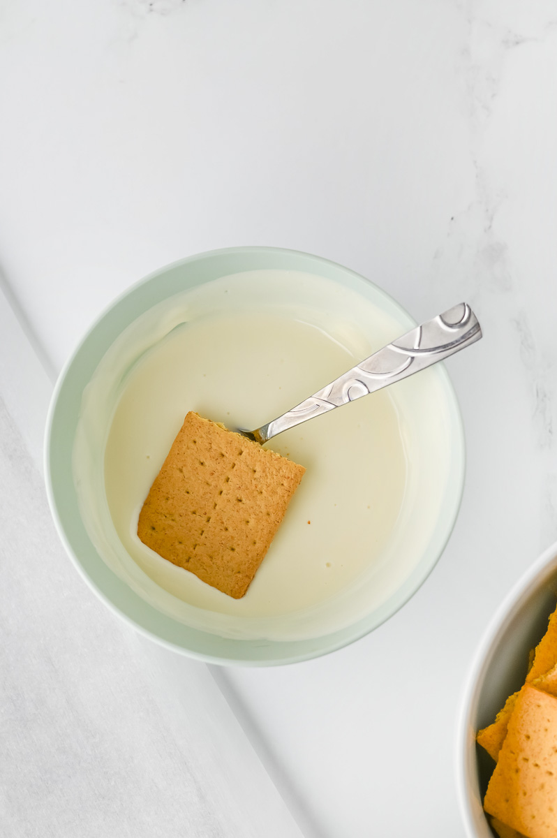 Graham crackers are dipped in melted chocolate.