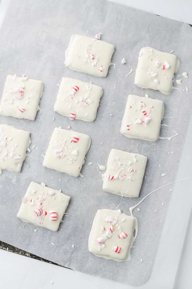 White chocolate-dipped Graham crackers on parchment-lined baking sheet sprinkled with crushed peppermint.