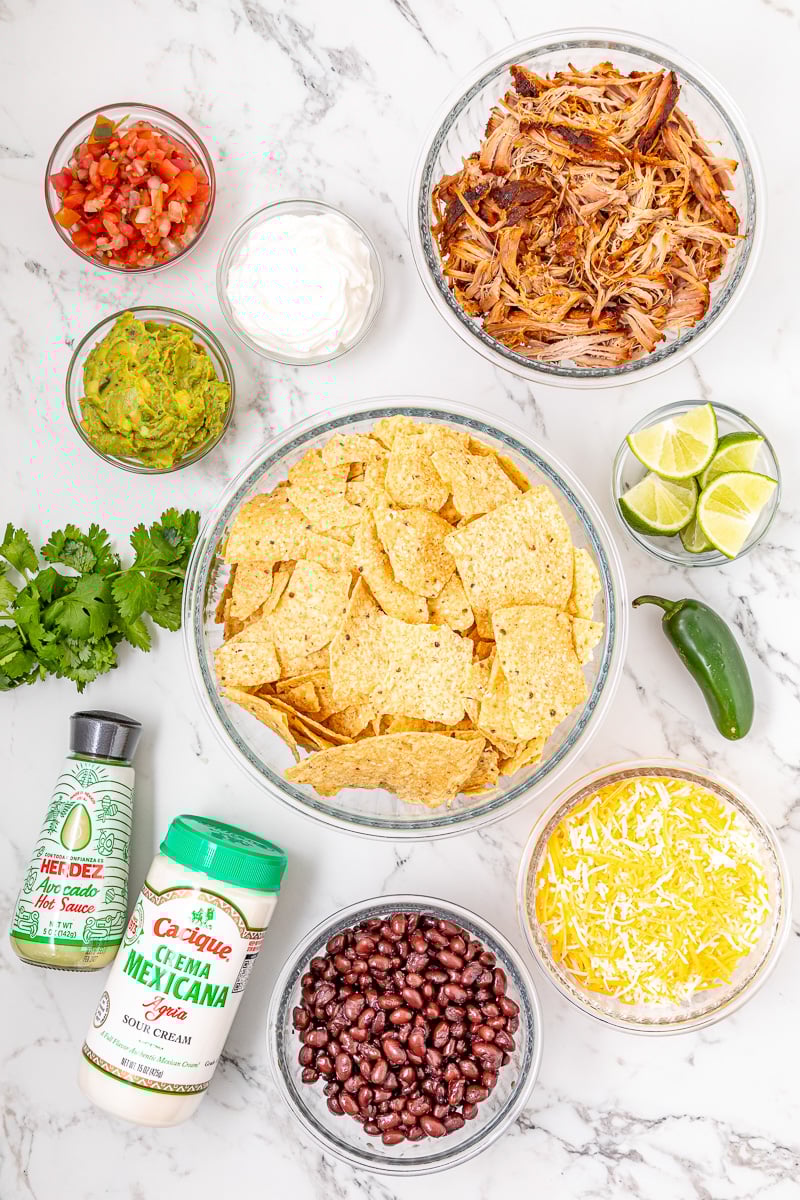 Ingredients for pulled pork nachos laid out on counter in small bowls.