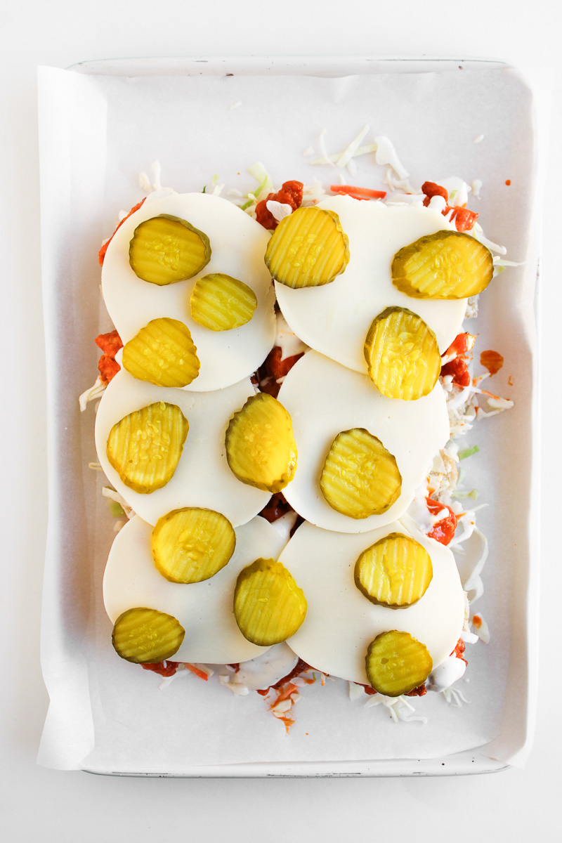 PIckles and cheese are added to the top of the sliders.