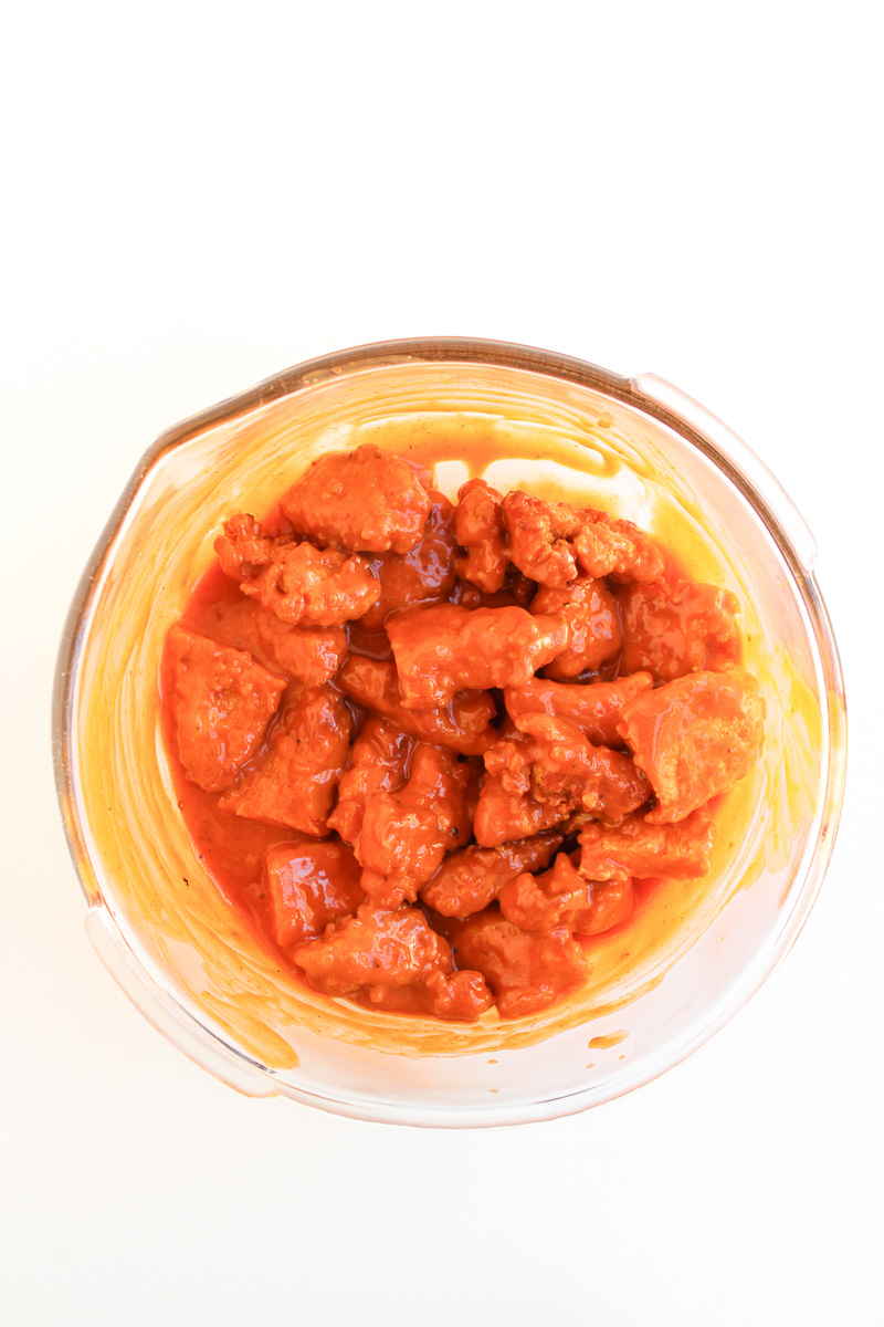 Chopped chicken is tossed in sauce in mixing bowl.