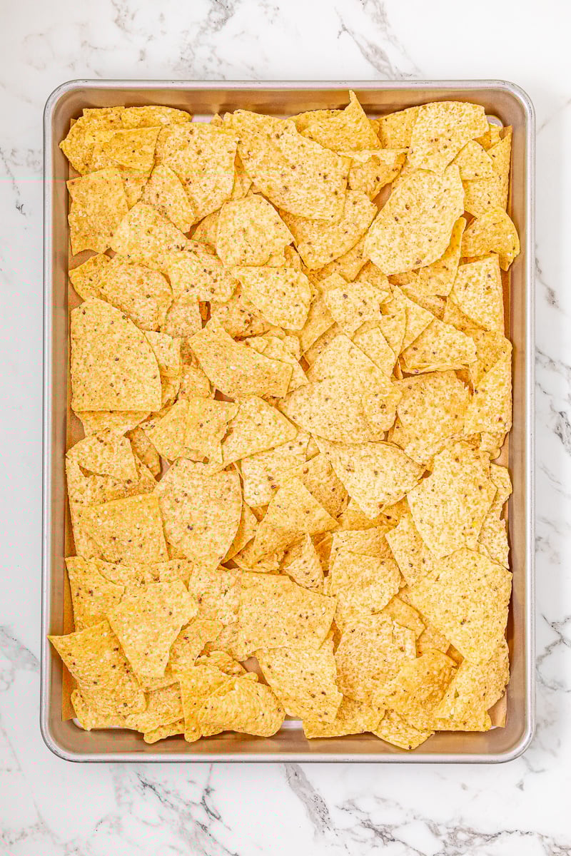 Nachos are spread out on baking sheet.