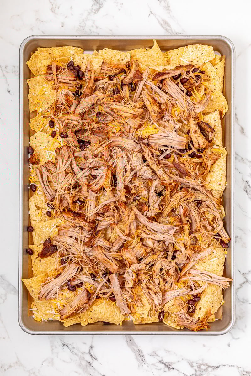 Pulled pork is sprinkled on top of the nachos.