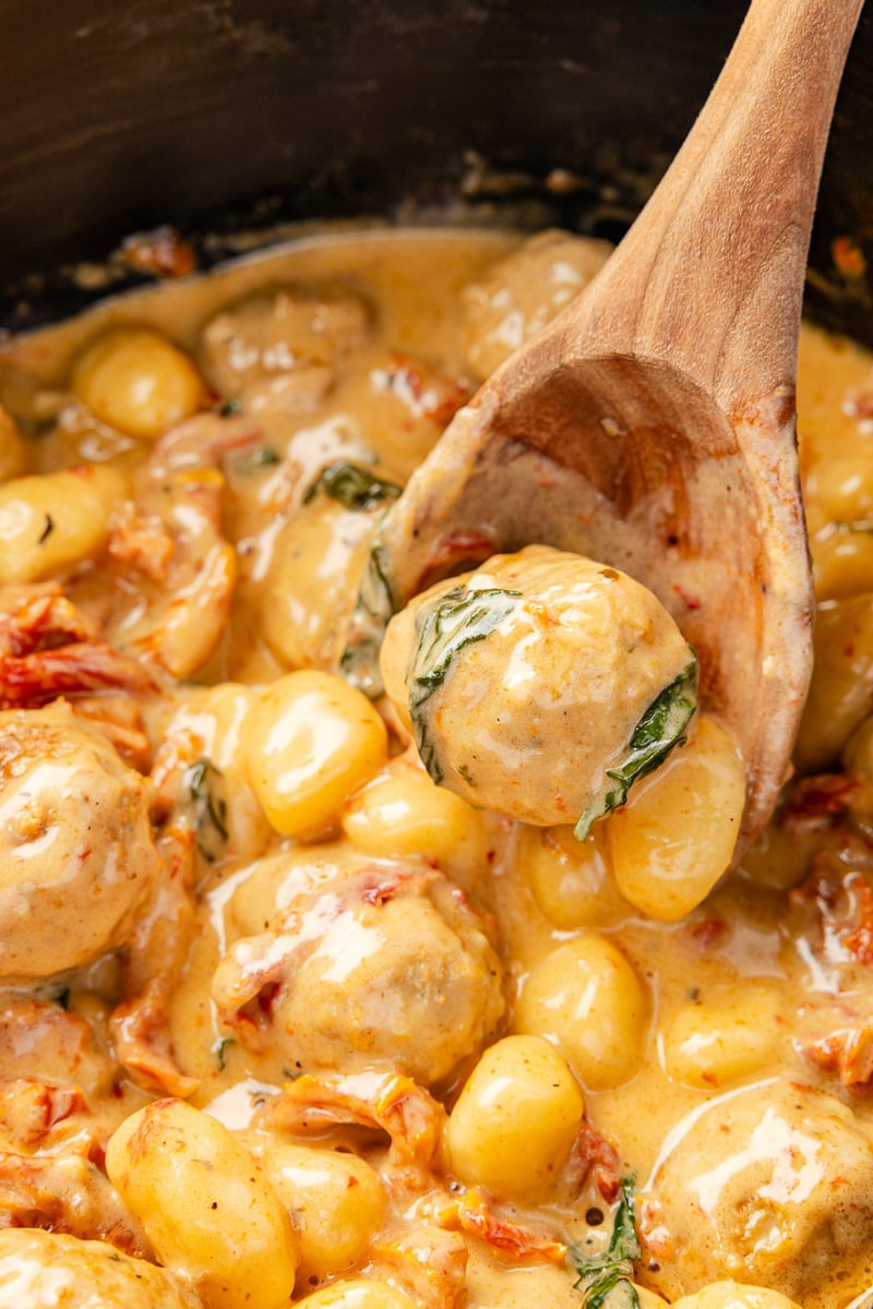 Close-up of slow cooker Tuscan chicken meatballs in creamy Parmesan sauce with gnocchi and spinach on a spoon