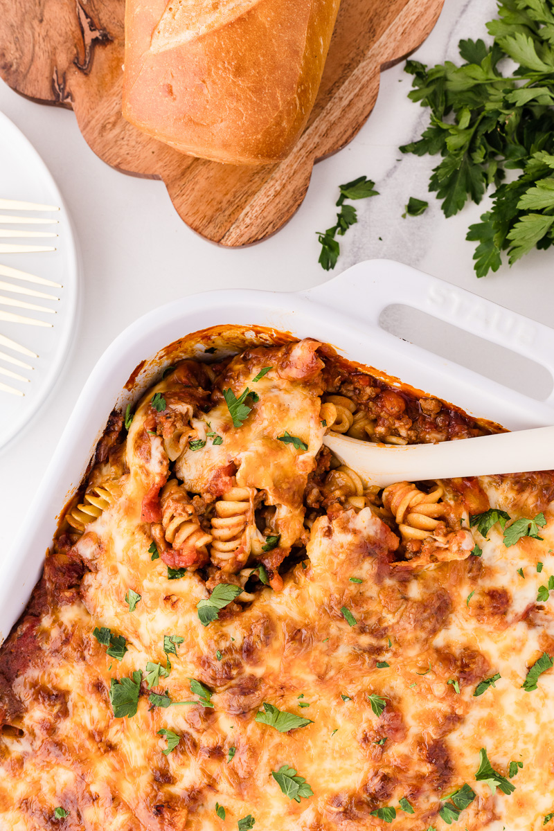 Scoop of bolognese pasta bake held over casserole dish.