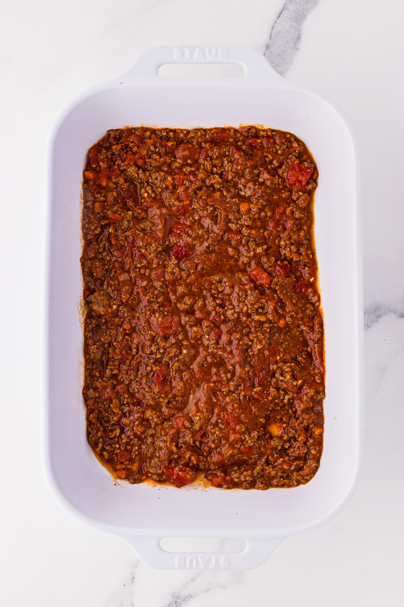 Bolognese sauce is spread into the bottom of casserole dish.