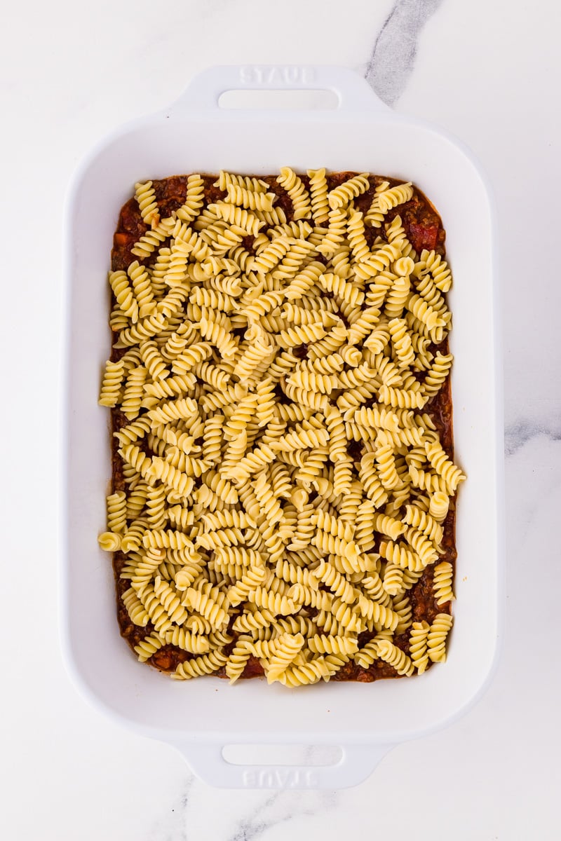 Rotini pasta is spread on top of the bolognese sauce.