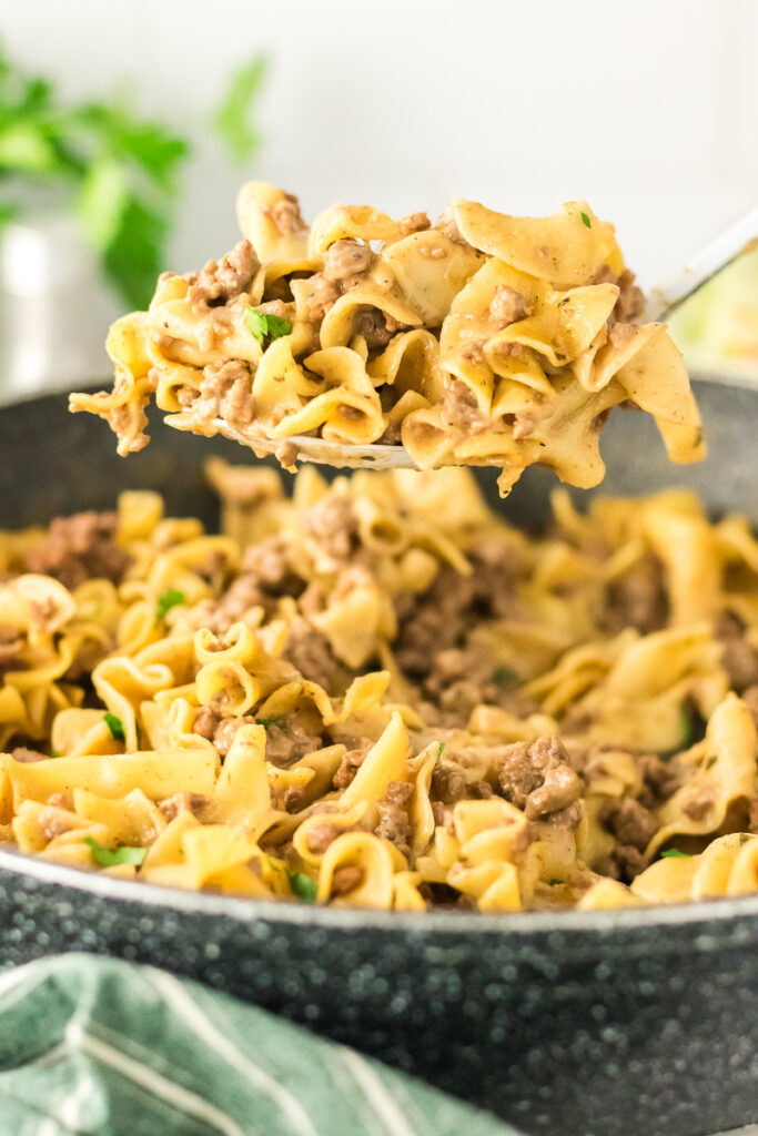 Homemade beef noodle hamburger helper scooped up with a spoon held over skillet.