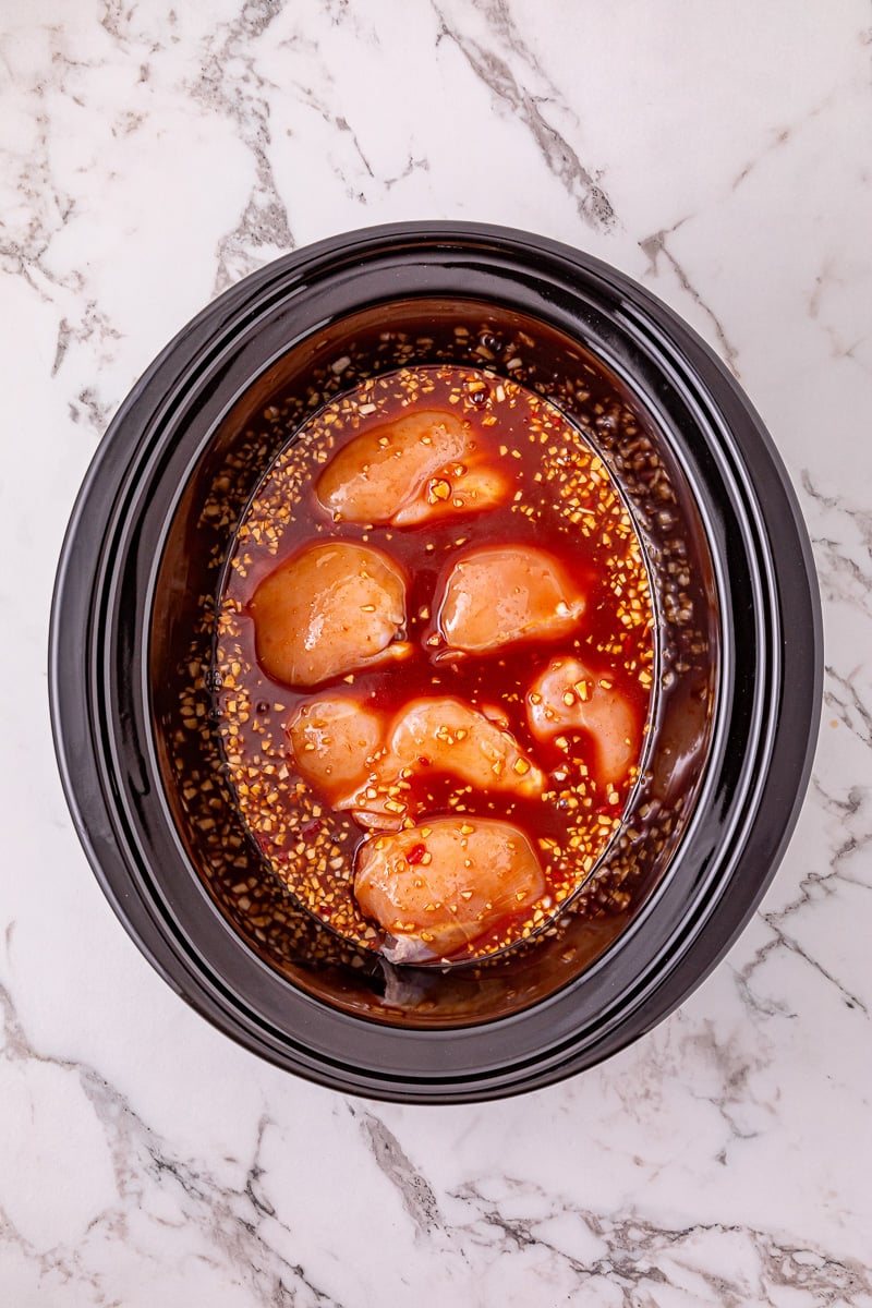 Sauce is poured over the chicken thighs in crockpot.