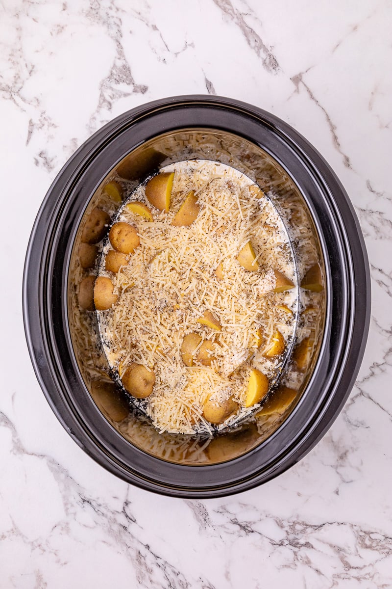 Shredded Parmesan cheese is sprinkled on top of the mixture in crockpot.