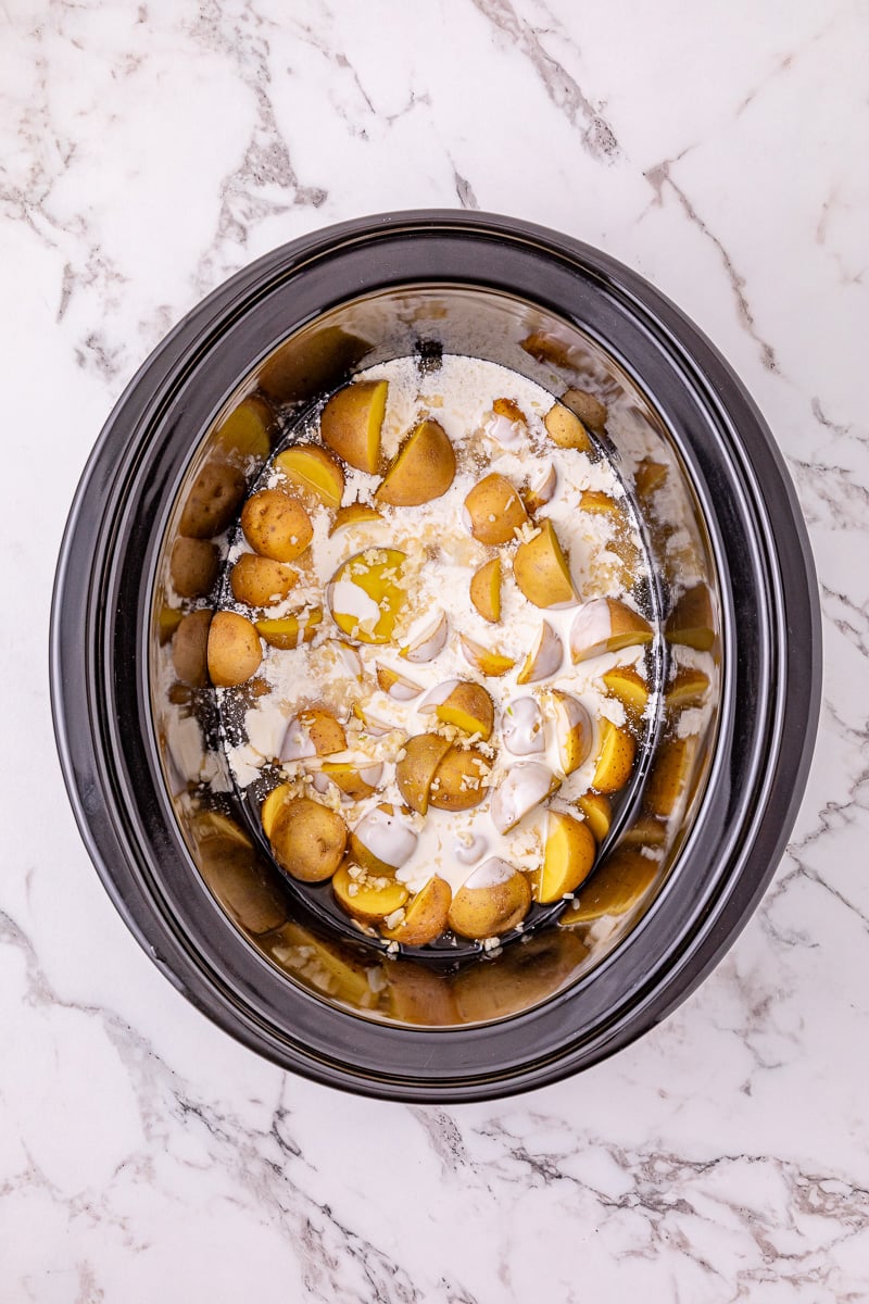 Potatoes and garlic and cream are added to the crockpot.