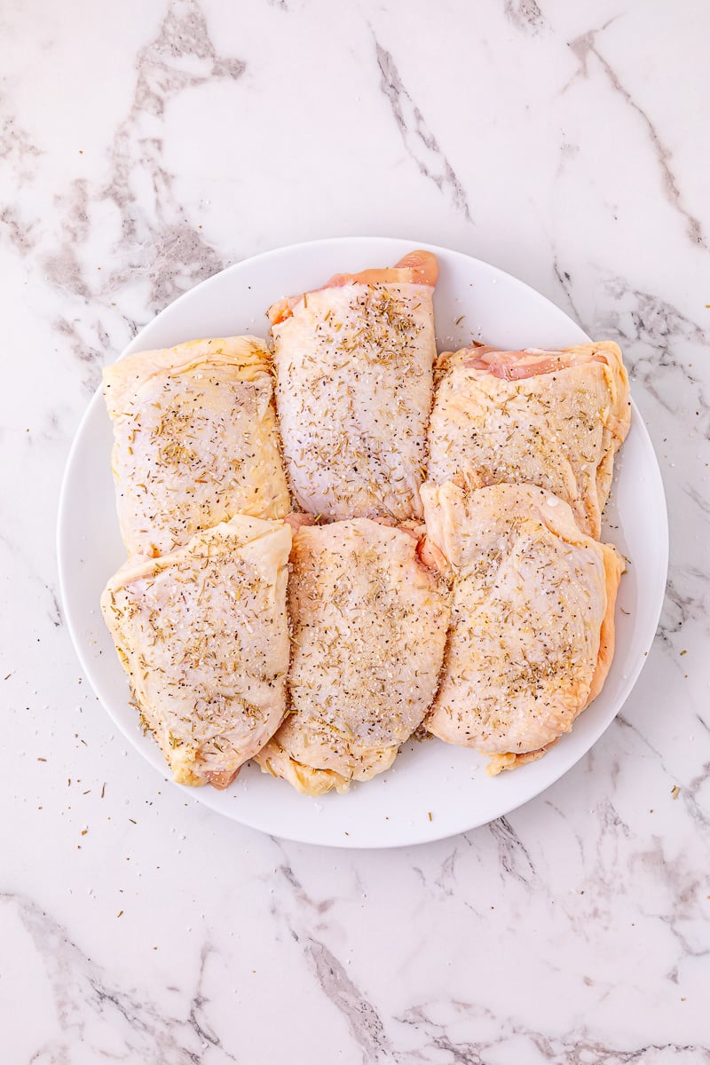 Herbs are sprinkled on bone-in chicken thighs on a plate.