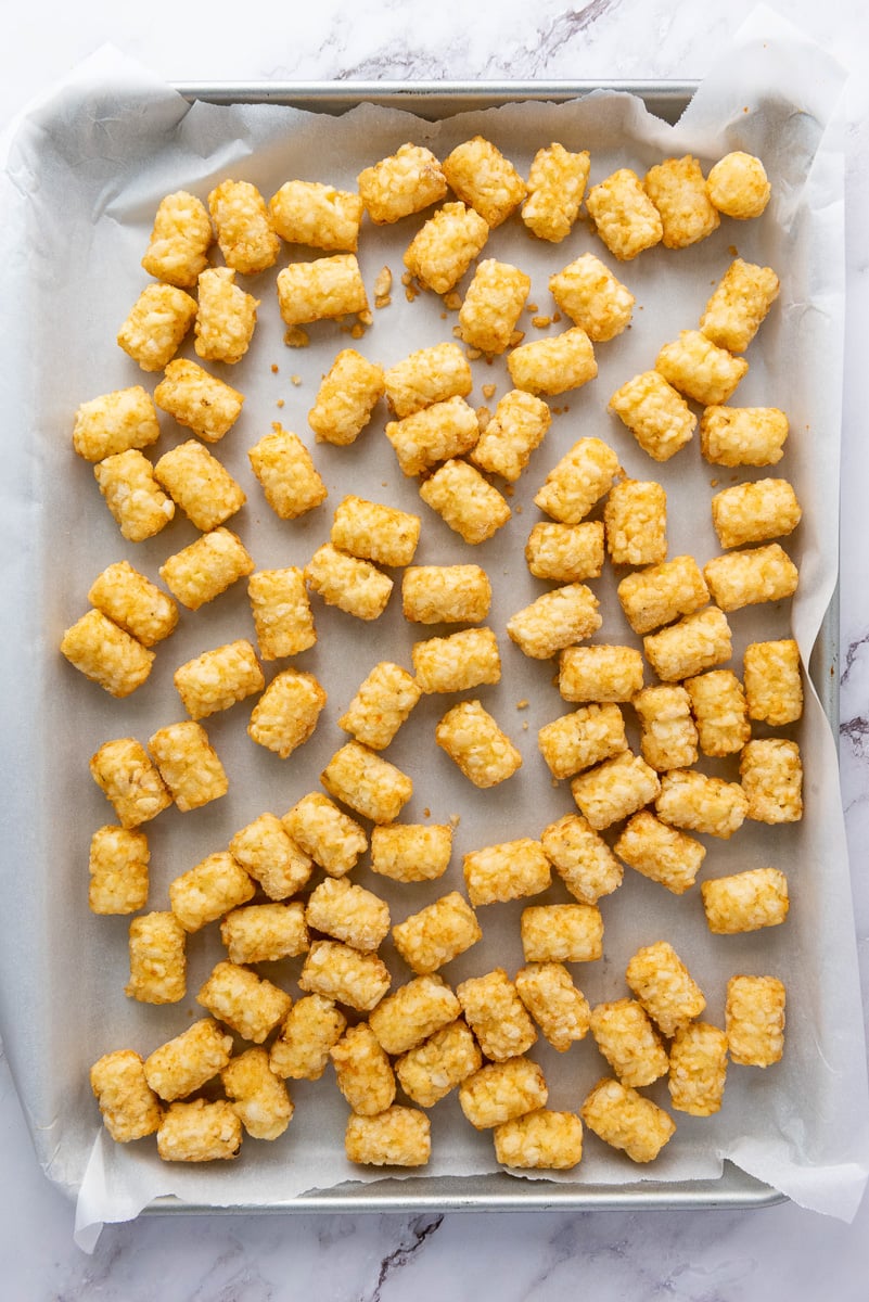 Tater tots spread in single layer on baking sheet ready to go into the oven.