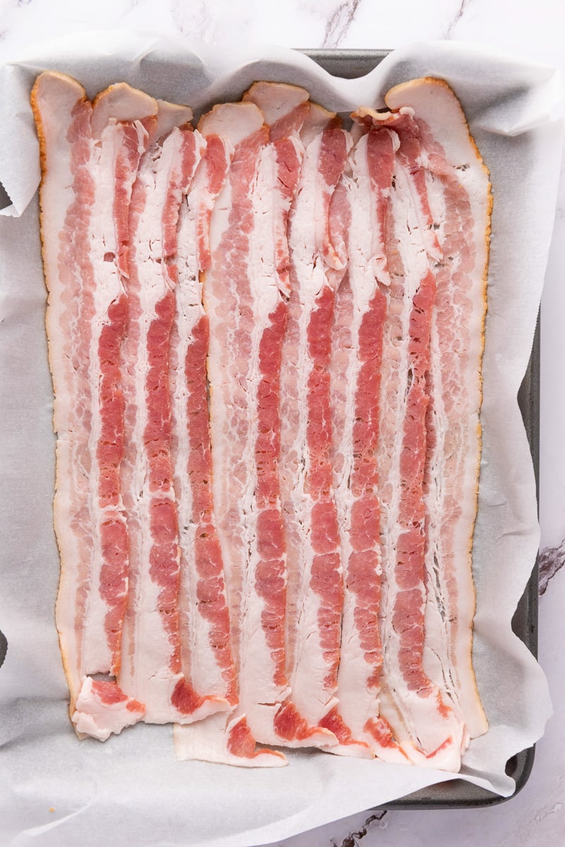Uncooked bacon on baking sheet ready for the oven.