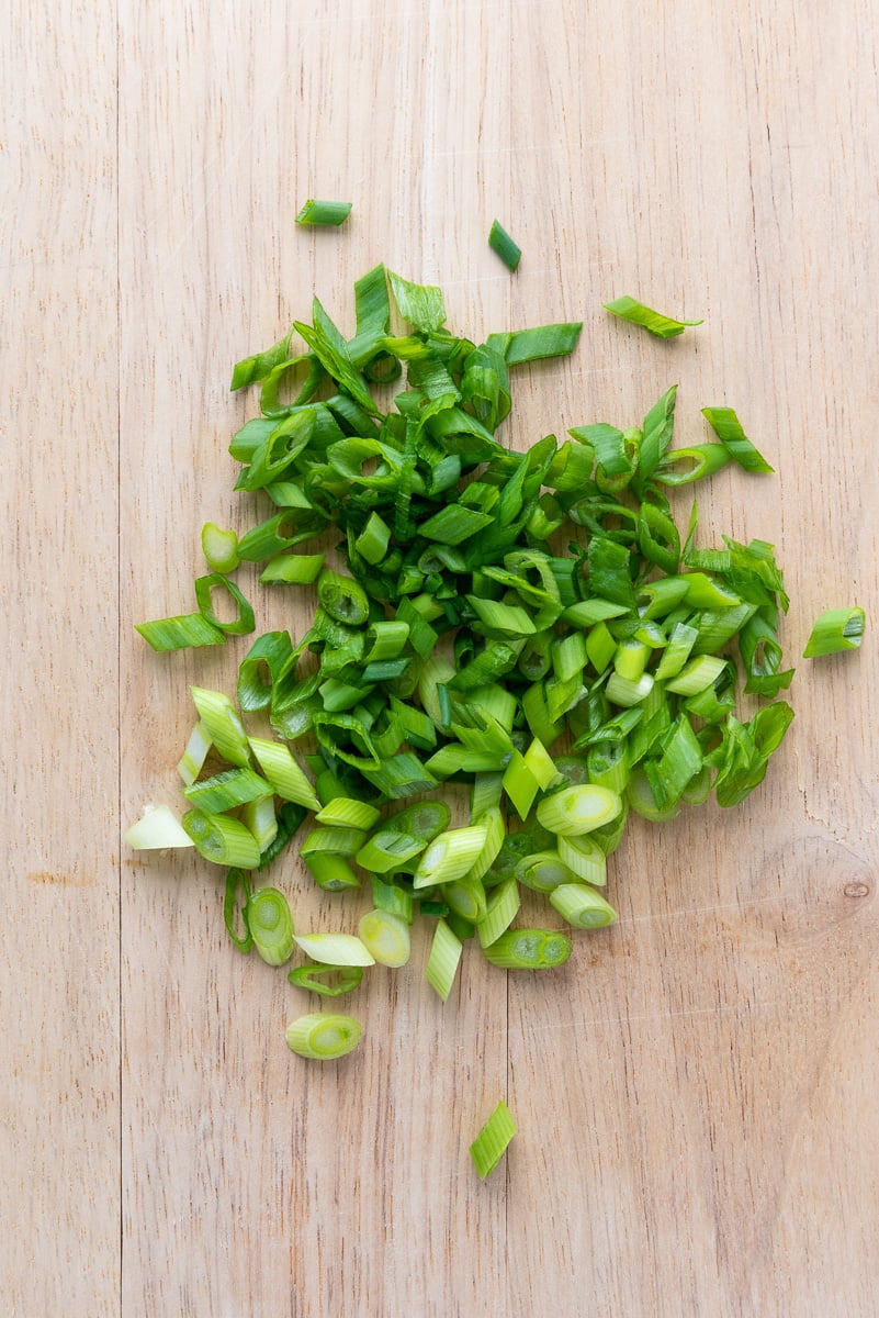 Sliced scallions on wooden cutting board.