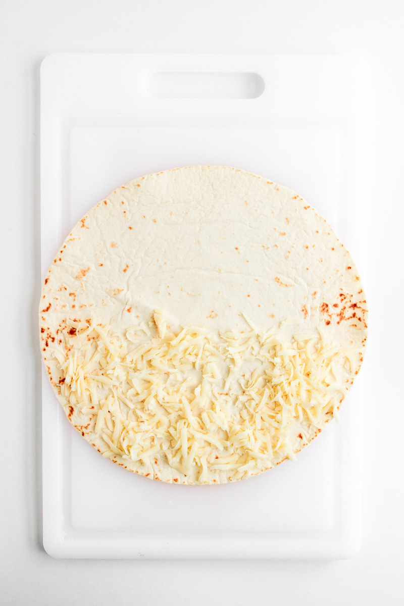 Mozzarella is sprinkled on half of the quesadilla.