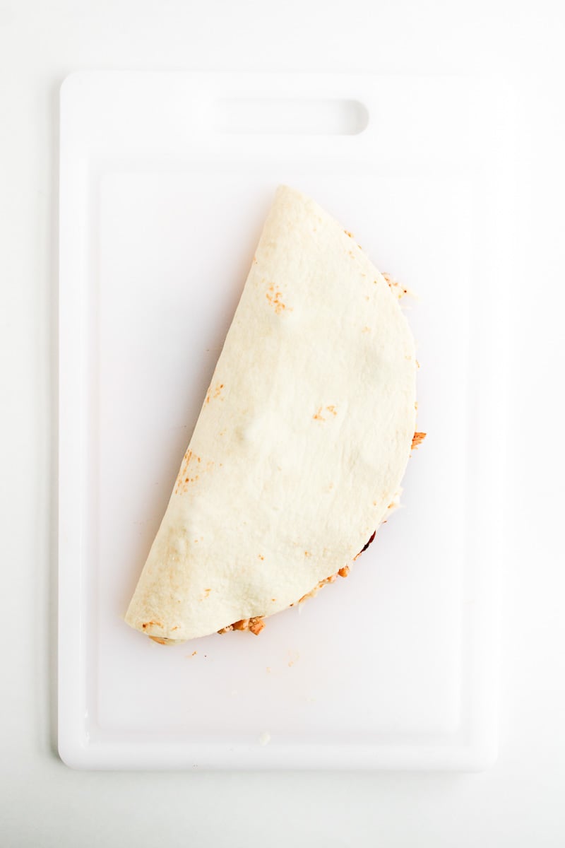 Folded quesadilla on white board ready to be grilled.