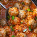 Crockpot enchilada meatballs scooped up in spoon held over slow cooker.