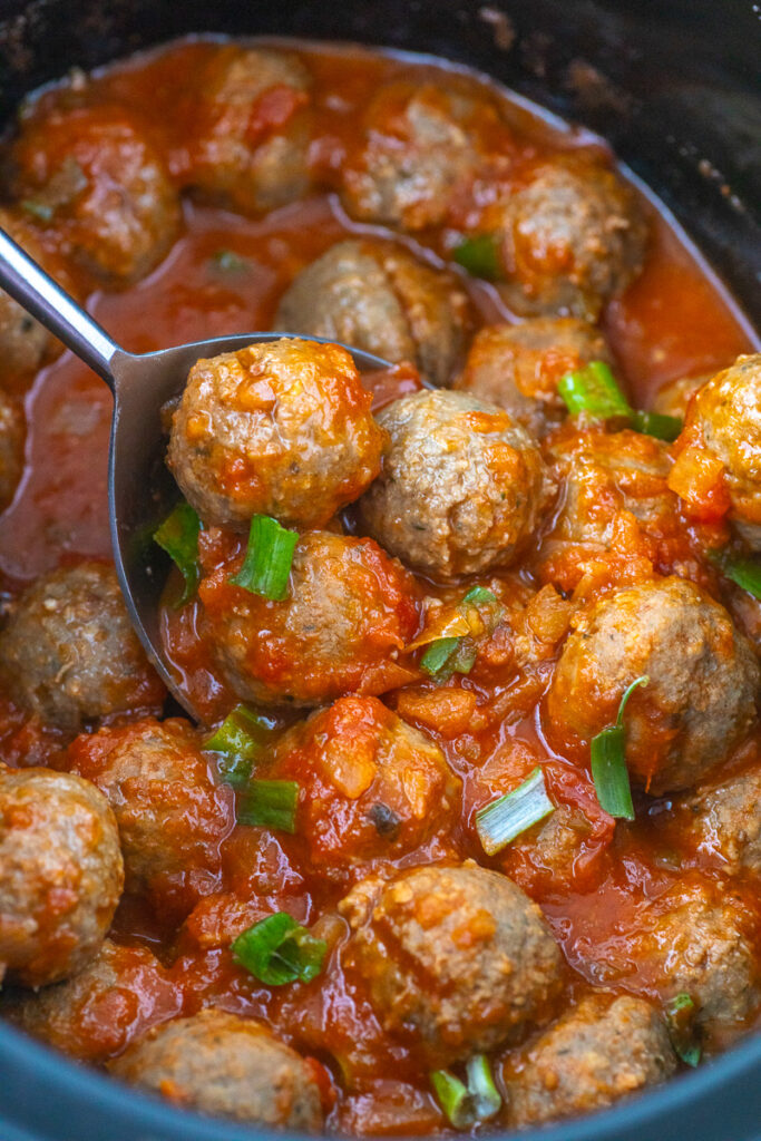 Crockpot enchilada meatballs scooped up in spoon held over slow cooker.
