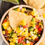 Pineapple mango salsa in a bowl with a nacho chip on top.