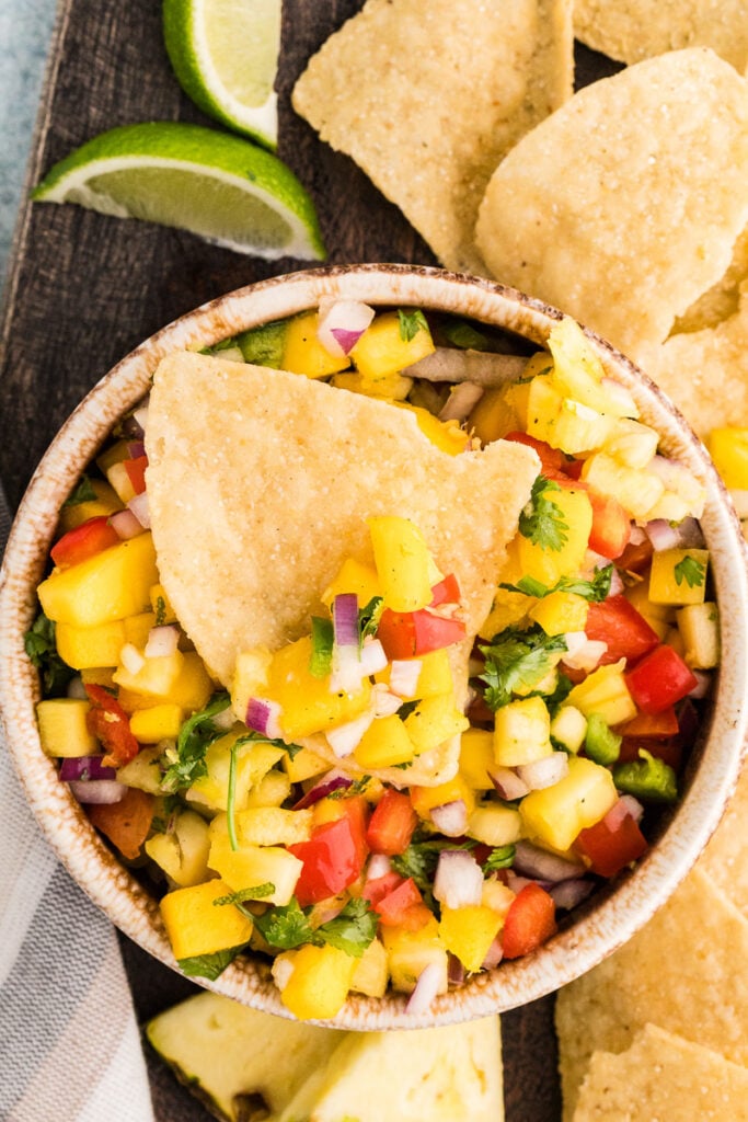 Pineapple mango salsa in a bowl with a nacho chip on top.